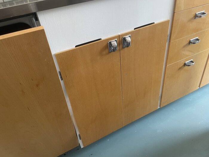 Träskåpsluckor i ett kök, med två luckor i mitten där användaren letar efter tips om barnsäkra lås, byggt med IKEA-stommar.