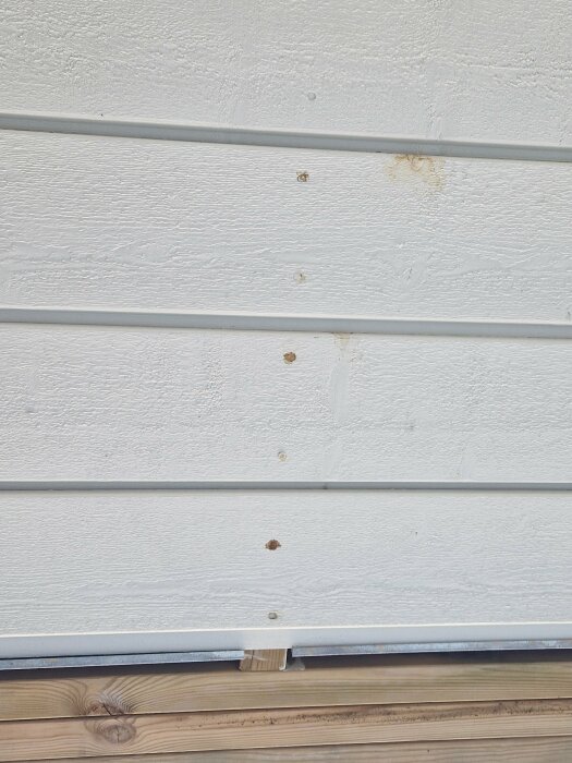 Rostfläckar och rostskador på vitmålade panelbrädor i ett undertak på en balkong.