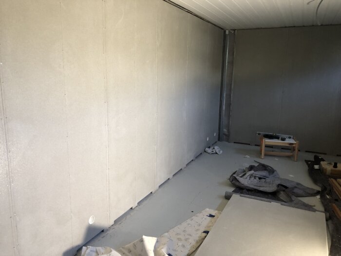 Rum med nyligen installerade fibercementskivor på väggarna, verktyg, byggmaterial och en arbetsbänk på golvet.