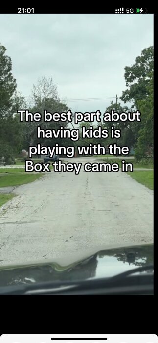 Vy från bil mot en lugn, trädkantad väg med texten "The best part about having kids is playing with the Box they came in" överlagrad.