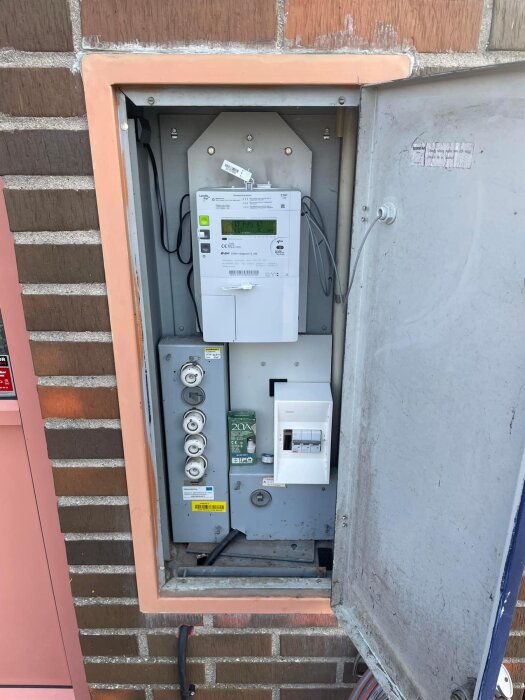 Elektrisk mätarskåp på en tegelvägg med nyinstallation av laddbox, kablar och säkringar synliga.