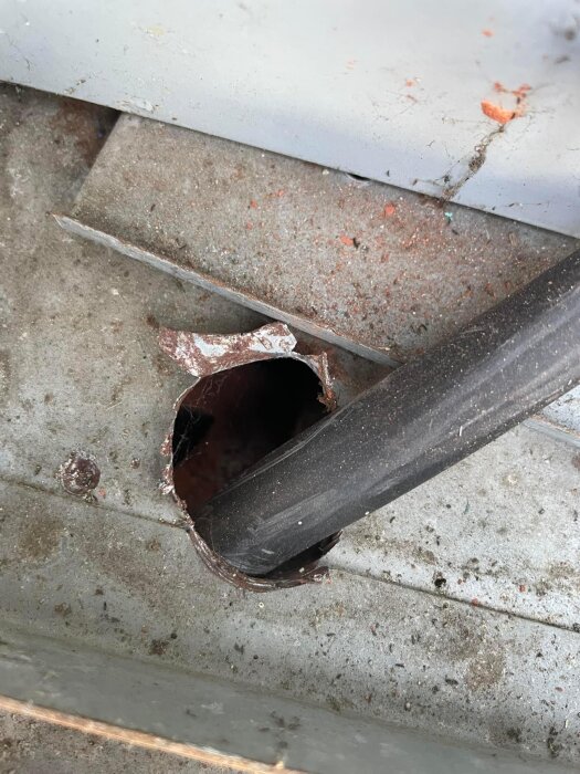 Svart kabel inmatad genom ett grovhugget hål i en metallfasad vid installation av en laddbox. Smuts och rost runt hålet.