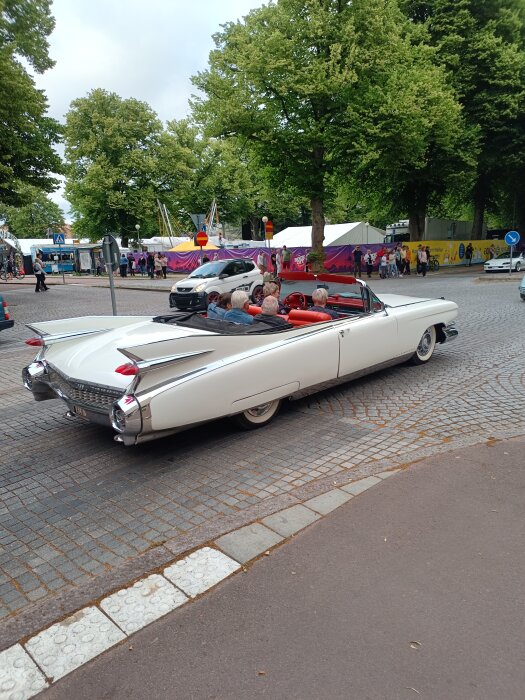 Vit Cadillac Eldorado Seville från 1959 med cabrioletutförande och röda säten, full med passagerare, syns på en stenlagd gata under Ålands cruisingevenemang.