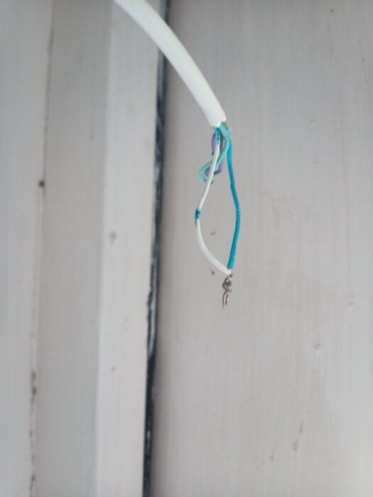 Två blå och en vit avskalad kabel hänger löst från väggen.
