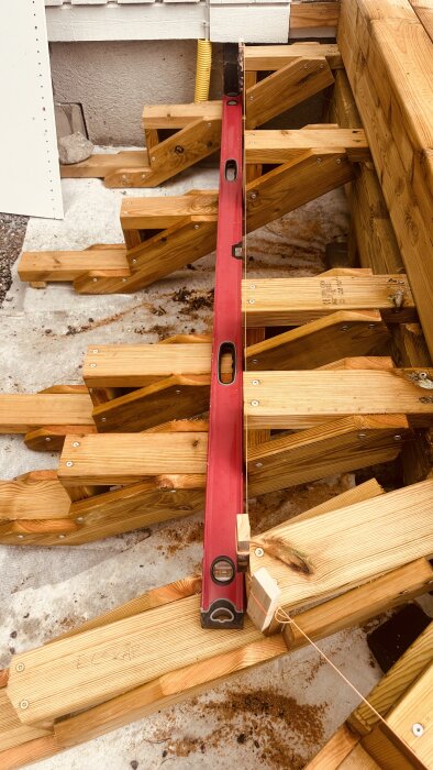 Trästomme för en altan eller trall med en röd vattenpass utplacerad för att justera träramarna i hörnen.
