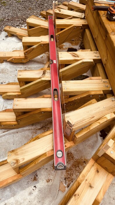 Trallprojekt med träkonstruktioner och en röd vattenpass på. Övre delen visar verktyg och grus.