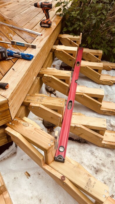 Trädäckprojekt med verktyg som skruvdragare, måttband och vattenpass. Visar justerade träramar redo för montering av trall.