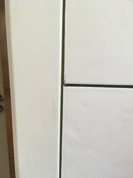 En närbild av en badrumsvägg där det saknas fog mellan kakel och dörrlist.
