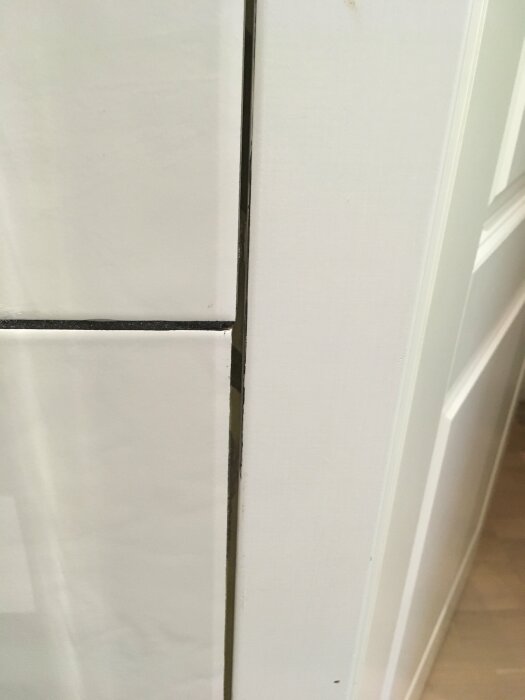 Närbild på badrumsvägg utan fogning mellan vita kakelplattor och dörrlist, vilket skapar ett gap där vatten kan tränga in och orsaka skador.
