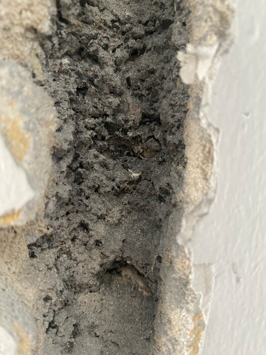 Närbild på en innervägg från 1936 med svart damm eller sot inuti väggen, möjlig misstanke om asbest.