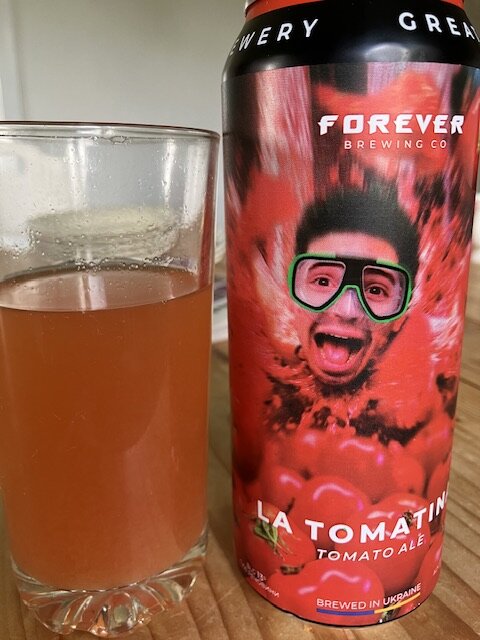 En ölburk med etiketten "La Tomatina Tomato Ale" från Forever Brewing Co och ett glas med en rödbrun dryck.