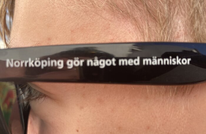 Närbild på ett ansikte med svart glasögonbåge där det står texten "Norrköping gör något med människor".