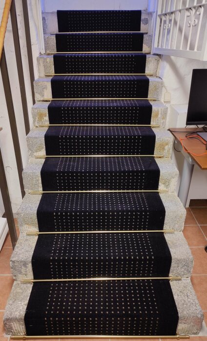 En stentrappa med mörk matta på varje trappsteg, fastsatt med mässingsstänger, förslag på renovering av trappan.
