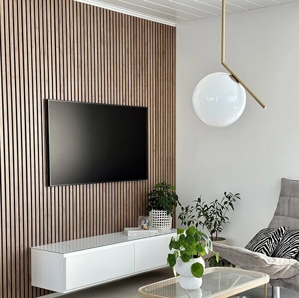 Vardagsrum med trävägg, monterad TV, modern lampa, vit TV-bänk och gröna växter i krukor.