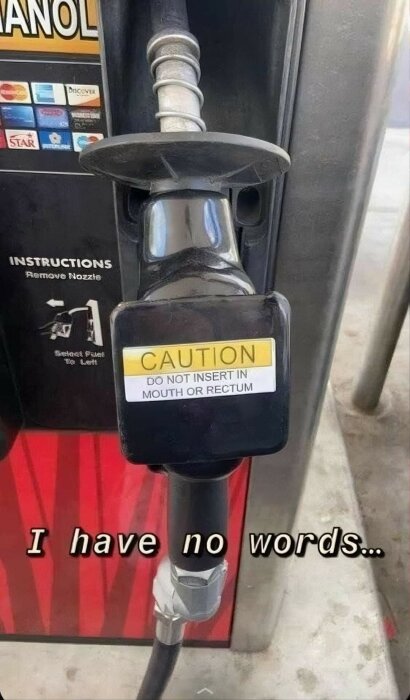 Närbild på ett bensinmunstycke på en pump med en varningsskylt som säger "FÖRSIKTIGHET: Sätt inte in i mun eller rektum" och texten "I have no words..." i bildens nederkant.