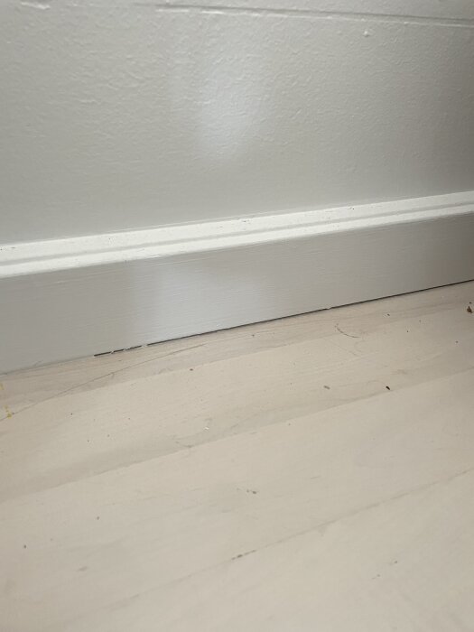 Glipa mellan golvsockel och golv på ett ostädat trägolv målat i vitt, med synlig separation mellan sockel och golvbräda.