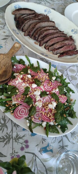 Flankstek serverad på fat och en sallad med ruccola, sparris, polkabeta, fetaost, pinjenötter och pesto på en tallrik.