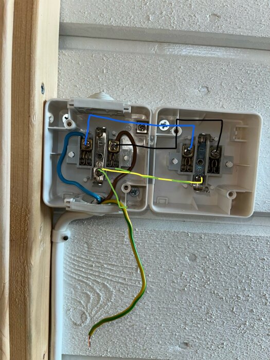 En kopplingsdosa med flera elektriska ledningar i olika färger anslutna till terminaler på en vägg av vitt träpanel.