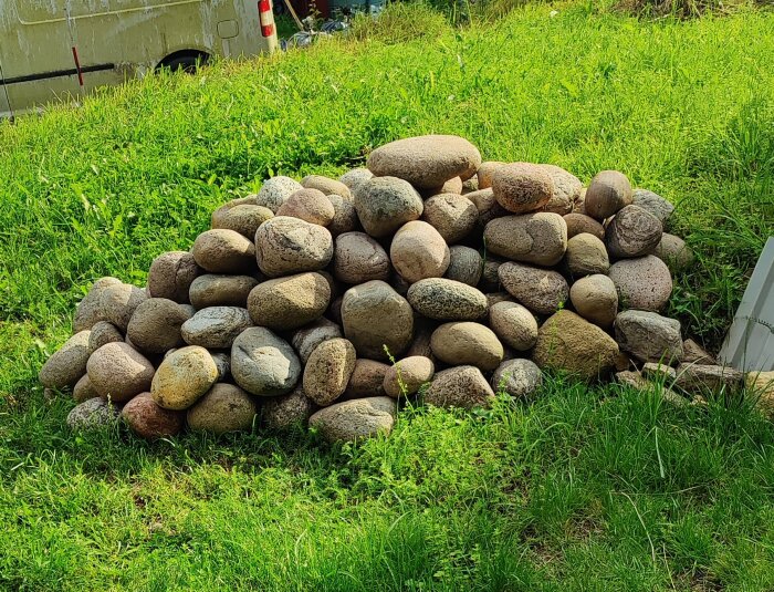 En hög med skrubbade stenar som ska användas till en stenmur, placerade på en gräsmatta, med en skåpbil i bakgrunden.