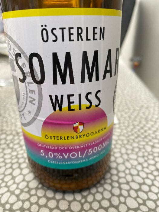 Närbild på etiketten av en flaska Österlen Sommar Weiss öl, 5.0% vol, 500 ml, från Österlenbryggarna.