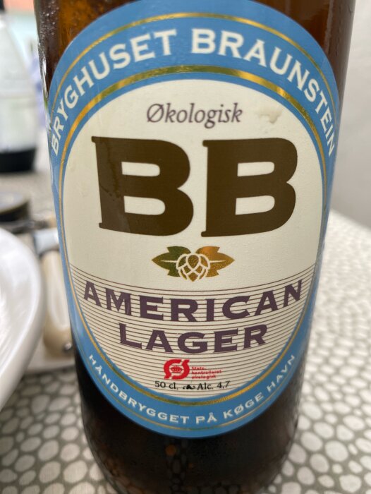 Närbild på en flaska Bryghuset Braunstein American Lager, en ekologisk öl med 4,7 % alkoholhalt, stående på ett bord under en ölprovning.