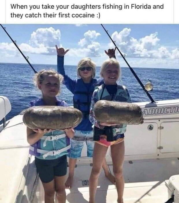 Tre barn i flytvästar på en båt håller stora paket och ler, med ett skämt om att de fångat kokain. Bakgrunden är ett hav med himmel och moln.