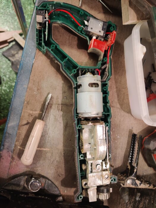 En isärskruvad Lidl/Parkside tigersåg med synliga elkomponenter, motor och växellåda. En skruvmejsel och annan utrustning ligger bredvid på arbetsbänken.