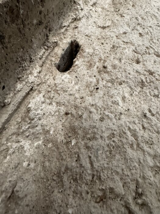 Hål i betonggolv som visar tecken på fuktskador, vilket kan observeras genom närvaron av gammalt trä inuti hålet i en gillestuga.