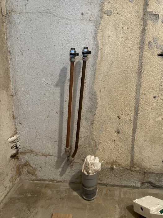Två rör med vattenledningar för varmt och kallt vatten installerade på betongvägg, avsedda för anslutning till en diskmaskin.
