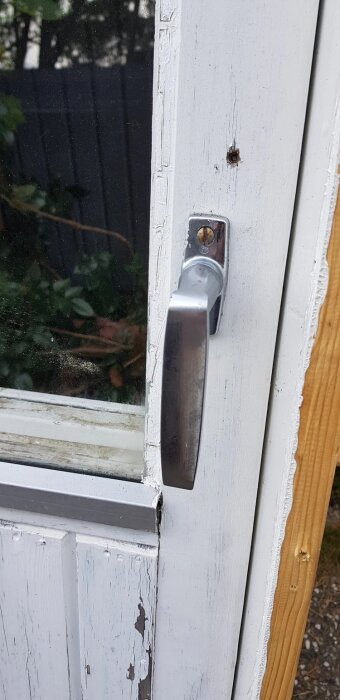 Närbild på ett handtag och låshus på en vit dörr, där låshuset är synligt och en skruvskalle är monterad bredvid ett litet hål.