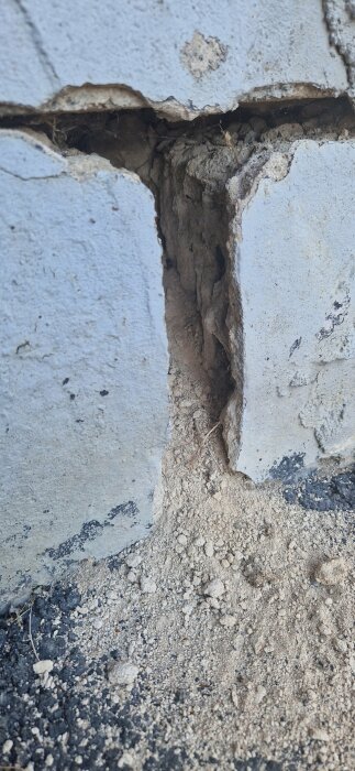 Närbild av ett sprucket betongblock med jord och småsten som har trillat ner över sprickan.