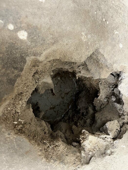 Ett närbildsfoto på en blöt fläck i en trasig betonggolvyta i en källare. Fuktig jord är synlig i det uppbilade hålet.