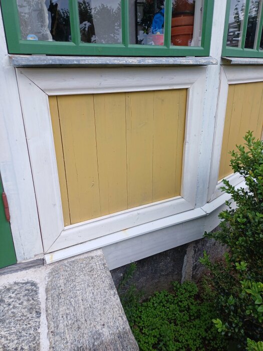 Närbild på en tambur som är grundmålad i vitt och gult med gröna fönsterkarmar; träpanel har tillverkats av gamla golvplankor och en egen bård är synlig.