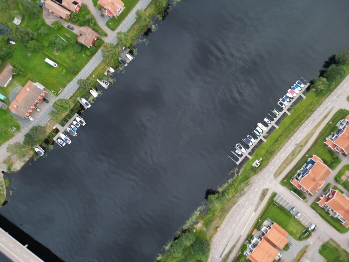 Flygbild av båtar förtöjda vid två kajer längs en flod, omgiven av hus och vägar.