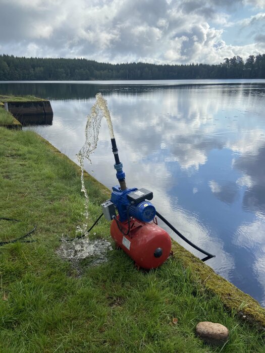 Elektrisk vattenpump på gräsmatta nära sjö, pumpar vatten uppåt.