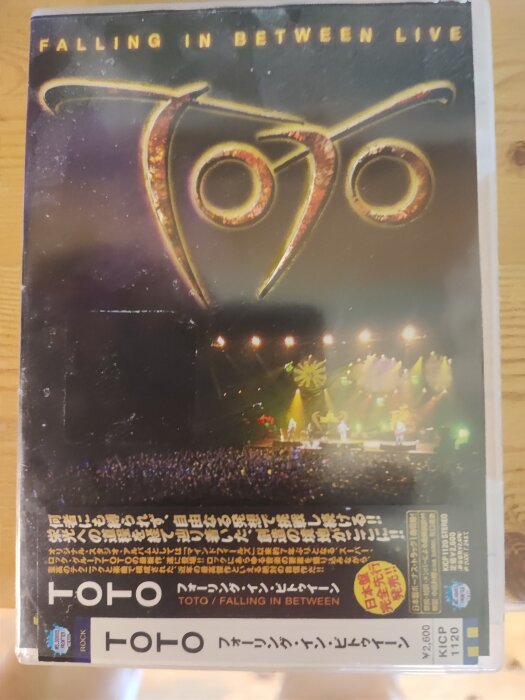 DVD-omslag för Toto-konserten "Falling in Between Live" med logotypen i guld ovanför en konsertbild och text på japanska.