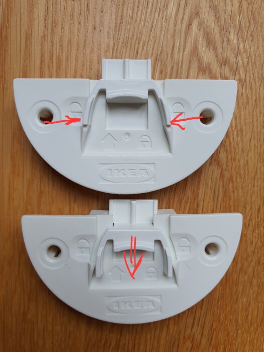 Vit låsmekanism från IKEA med röda pilar som visar hur man trycker ihop bågen för att dra spärren nedåt.
