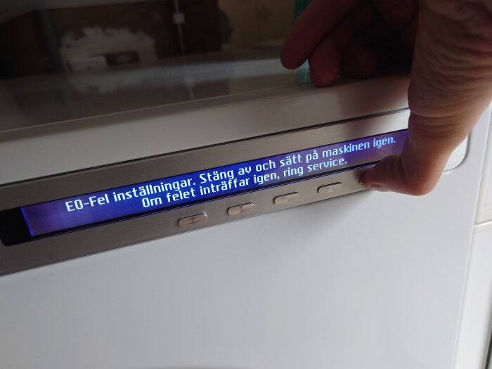 Display på tvättmaskin visar felmeddelande "EO-Fel inställningar" och uppmanar att stänga av och sätta på maskinen igen. En hand trycker på knapp.