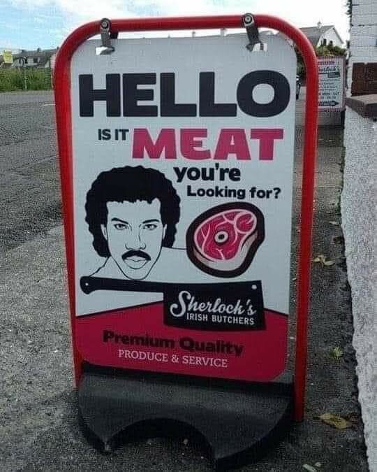 Reklamskylt utanför en slaktare med texten "HELLO IS IT MEAT you're Looking for?" tillsammans med en tecknad bild av ett ansikte och en köttbit. Märkt Sherlock's Irish Butchers.