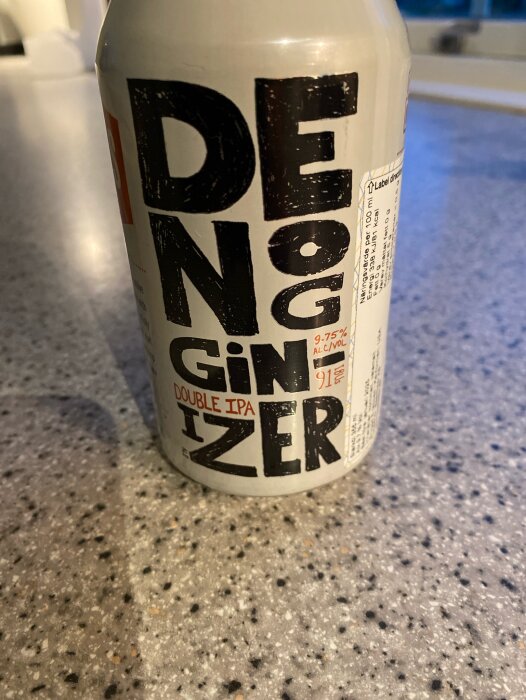 En burk med texten "DENOGGINIZER DOUBLE IPA" står på en gråmelerad köksbänk, med alkoholhalten 9,75% synlig på etiketten.