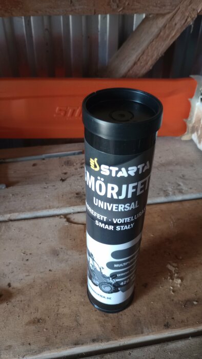 Ett rör med Starta smörjfett universal, placerat på en träyta med en orange detalj i bakgrunden.