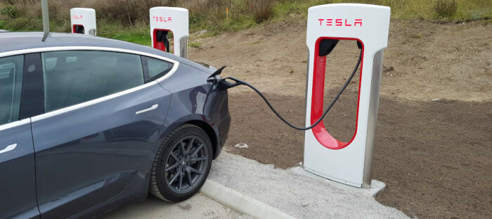 En elbil av märket Tesla laddar vid en laddstation utomhus.