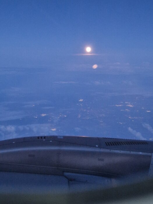 Fullmåne den 21 juli fotograferad från ett flygplan med utsikt över moln och nattsken nedanför.