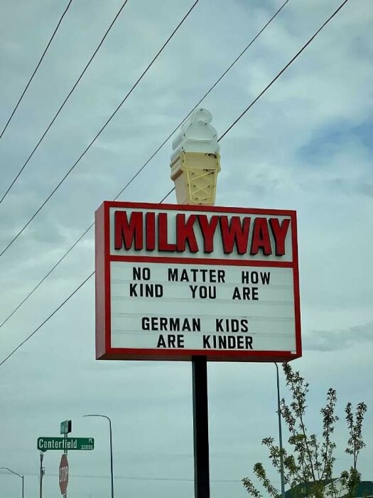 Röd och vit skylt som tillhör "Milkyway" glassbutik med texten "No matter how kind you are, German kids are kinder" mot en molnig himmel och en stoppskylt i bakgrunden.