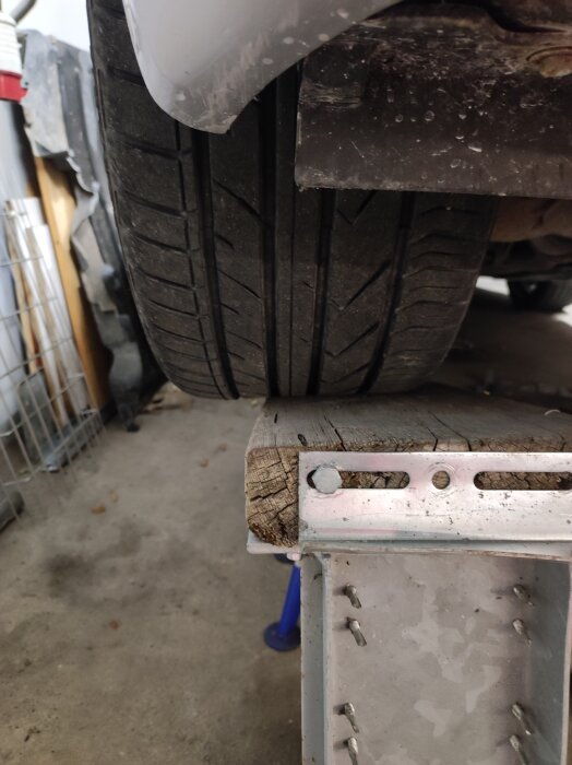 Närbild av ett sommarhjul på en bil som står på en ramp, med en träregel och metallbeslag under hjulet.