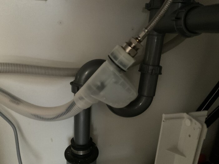 Diskmaskinens Aquastop-ventil och vattenanslutningar under diskbänken, med slangar, rör och kopplingar synliga.