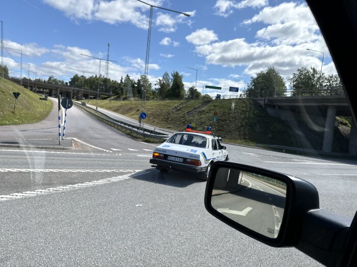 Polisbil kör i en rondell under en motorvägsbro på en solig dag.