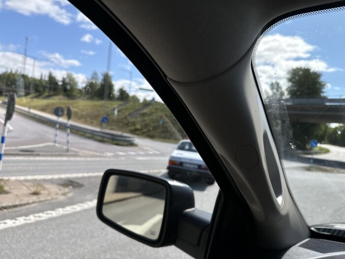 Bilden visar en trafikplats sedd från insidan av en bil genom sidorutan, tagen på en solig dag.