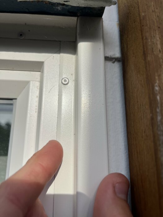 Närbild på vit plåt i fönsterkarm med en persons finger som pekar på kanten av plåten.