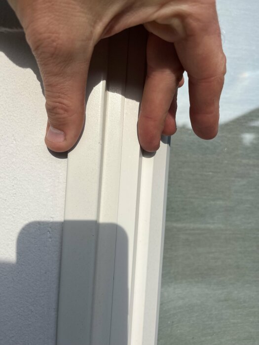 En hand håller i en vit, smal metallplåt fäst vid en vägg.